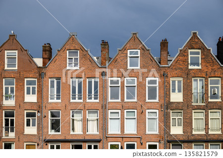 Row of traditional European brick houses with gabled roofs in Amsterdam, Netherlands Row of traditional European brick houses with gabled roofs in Amsterdam, Netherlands 135821579