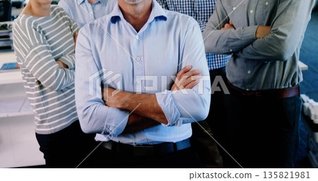 Standing corporate team leader in light blue shirt crossing arms in open office with white desks Standing corporate team leader in light blue shirt crossing arms in open office with white desks 135821981