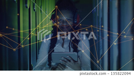 IT engineer analyzing network graph in LED-lit server rack aisle, with tablet, red headphones 135822094