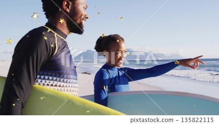 Standing surfers wearing wetsuits holding surfboards on sandy shore, pointing toward ocean horizon Standing surfers wearing wetsuits holding surfboards on sandy shore, pointing toward ocean horizon 135822115