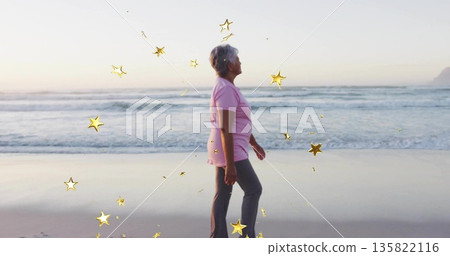 Walking woman in pink polo and gray pants on sand at sunset, with digital star overlays 135822116