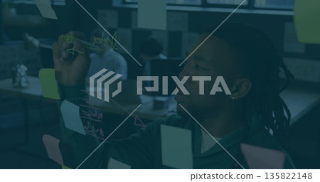 Black man marking glass partition in open-plan office, with marker, pastel sticky notes, copy space Black man marking glass partition in open-plan office, with marker, pastel sticky notes, copy space 135822148