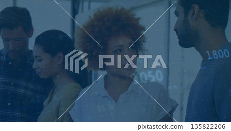 Talking woman with curly hair in white blouse presenting data on wall in office, digital overlay 135822206