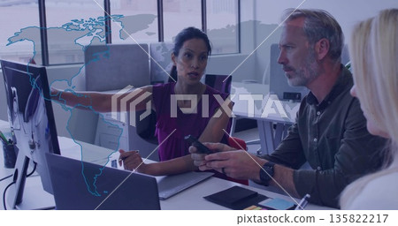 Business professionals reviewing world map on monitor in office, with laptop and smartphone Business professionals reviewing world map on monitor in office, with laptop and smartphone 135822217