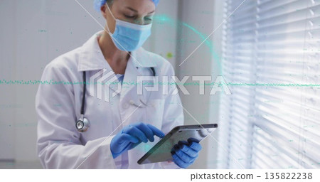 Tapping tablet female doctor wearing lab coat, mask and gloves in clinic, with stethoscope Tapping tablet female doctor wearing lab coat, mask and gloves in clinic, with stethoscope 135822238