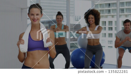 Fitness instructor wearing sportswear leading squat class in studio, with towel and stability balls 135822281
