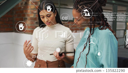Reviewing tablet, two women pointing stylus at floating CO2 charts and code in brick office 135822290