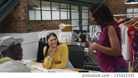Collaborating designers sketching garment patterns around studio table, with sewing tape and coffee 135822291