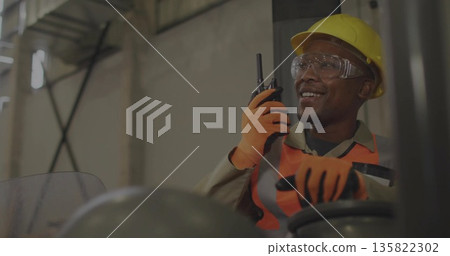 Operating forklift operator wearing safety gear holding walkie-talkie inside warehouse, copy space 135822302