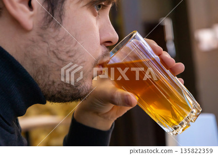 Young man drinking dried fruit compote from glass mug. Healthy drink for refreshment and hydration. Young man drinking dried fruit compote from glass mug. Healthy drink for refreshment and hydration. 135822359