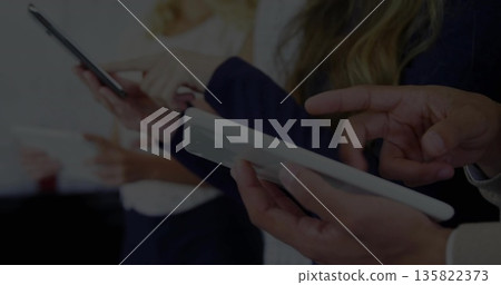 Standing four professionals in business attire holding smartphones and tablets in meeting room 135822373