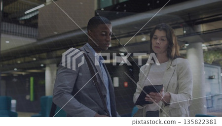 Two business colleagues reviewing tablet in transit station, with shoulder bag and blue chairs Two business colleagues reviewing tablet in transit station, with shoulder bag and blue chairs 135822381
