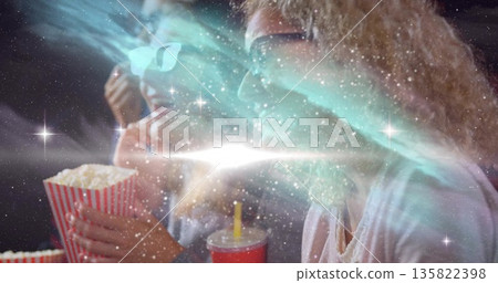 Holding popcorn, red cup, two women wearing 3D glasses watching movie under cosmic light at theater Holding popcorn, red cup, two women wearing 3D glasses watching movie under cosmic light at theater 135822398