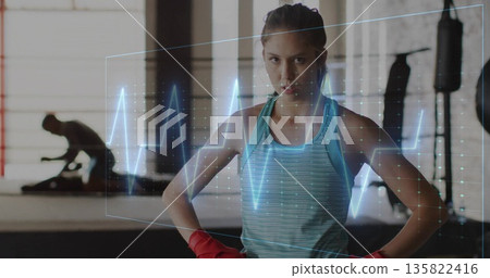 Standing female boxer in teal tank with red gloves in boxing gym, with ECG waveform overlay 135822416