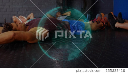 Projecting holographic globe hovering above six exercisers resting on gym floor with earphones 135822418