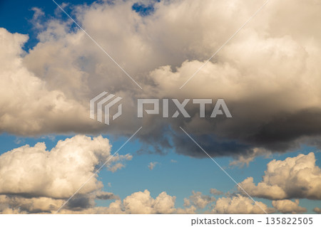 Fluffy cumulus clouds against a clear blue sky, illuminated by warm sunset light. Natural background for weather forecast or beautiful sky scene. Fluffy cumulus clouds against a clear blue sky, illuminated by warm sunset light. Natural background for weather forecast or beautiful sky scene. 135822505
