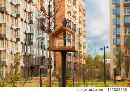 A wooden bird feeder in the courtyard of a modern apartment complex. Family, housing, mortgage, affordable credit 135822508