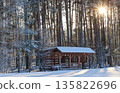 Wooden gazebo standing in a snowy winter forest capturing warm sunlight through pine trees on a cold morning 135822696