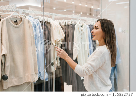 Smiling Woman Pointing at Beige Clothing Set in Store Window Smiling Woman Pointing at Beige Clothing Set in Store Window 135822757