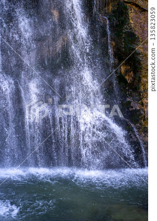 Powerful waterfall cascading down rocky cliff into clear mountain pool Powerful waterfall cascading down rocky cliff into clear mountain pool 135823059