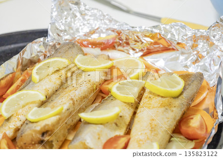 Prerape raw spiced hake for a bake in the oven with lemon, tomatoes, carrots, and onions in foil. Delicious fish for lunch or dinner, perfect for a diet. Tasty and fresh  hake fish for bake with 135823122