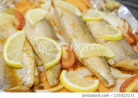 Prerape raw spiced hake for a bake in the oven with lemon, tomatoes, carrots, and onions in foil. Delicious fish for lunch or dinner, perfect for a diet. Tasty and fresh  hake fish for bake with 135823131