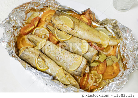 Spiced hake baked in the oven with lemon, tomatoes, carrots, and onions in foil. Delicious fish for lunch or dinner, perfect for a diet. Tasty hake fish baked with vegetables. Spiced hake baked in the oven with lemon, tomatoes, carrots, and onions in foil. Delicious fish for lunch or dinner, perfect for a diet. Tasty hake fish baked with vegetables. 135823132
