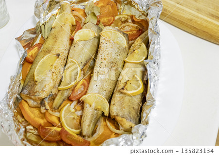 Spiced hake baked in the oven with lemon, tomatoes, carrots, and onions in foil. Delicious fish for lunch or dinner, perfect for a diet. Tasty hake fish baked with vegetables. Spiced hake baked in the oven with lemon, tomatoes, carrots, and onions in foil. Delicious fish for lunch or dinner, perfect for a diet. Tasty hake fish baked with vegetables. 135823134