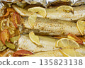 Spiced hake baked in the oven with lemon, tomatoes, carrots, and onions in foil. Delicious fish for lunch or dinner, perfect for a diet. Tasty hake fish baked with vegetables. 135823138