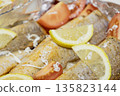 Prerape raw spiced hake for a bake in the oven with lemon, tomatoes, carrots, and onions in foil. Delicious fish for lunch or dinner, perfect for a diet. Tasty and fresh  hake fish for bake with 135823144
