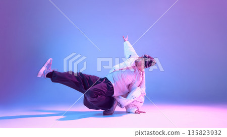 Street dancer holding low balance pose with raised arm in studio lighting. 135823932