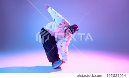 Male street dancer stretching leg while balancing in studio with blue purple light 135823934