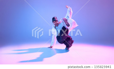 Street dancer performing high kick in studio with colorful lighting. Street dancer performing high kick in studio with colorful lighting. 135823941