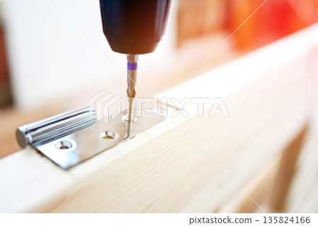 Screwdriver is used to attach hinge to wooden door frame. Cordless drill Screwdriver is used to attach hinge to wooden door frame. Cordless drill 135824166