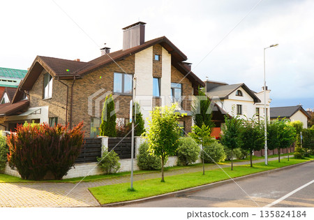 Street in residential area in suburb. Rows houses along road, sidewalk. Family house outside city. Street in residential area in suburb. Rows houses along road, sidewalk. Family house outside city. 135824184