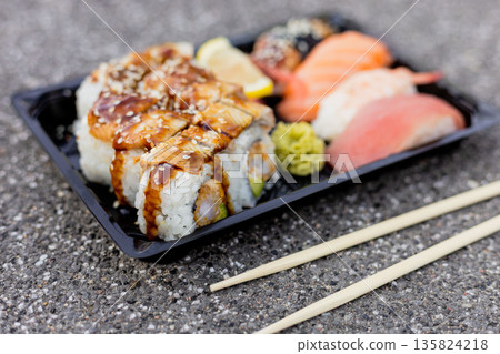 A carefully arranged sushi platter showcases various rolls topped with sauce and pieces of sashimi. The vibrant colors and textures are appealing, served with chopsticks A carefully arranged sushi platter showcases various rolls topped with sauce and pieces of sashimi. The vibrant colors and textures are appealing, served with chopsticks 135824218