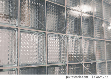 A wall made of clear glass blocks showcases unique textured surfaces that play with light. The design enhances the modern style of the room, creating a bright atmosphere A wall made of clear glass blocks showcases unique textured surfaces that play with light. The design enhances the modern style of the room, creating a bright atmosphere 135824233