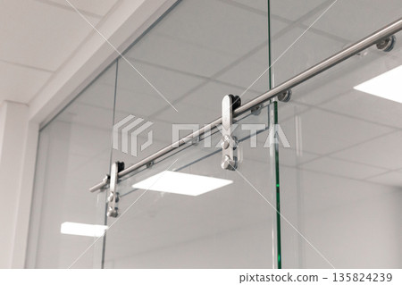 A sleek sliding glass door system showcases chrome hardware in a contemporary office. The well-lit environment highlights the clean lines and minimalistic design of the space A sleek sliding glass door system showcases chrome hardware in a contemporary office. The well-lit environment highlights the clean lines and minimalistic design of the space 135824239