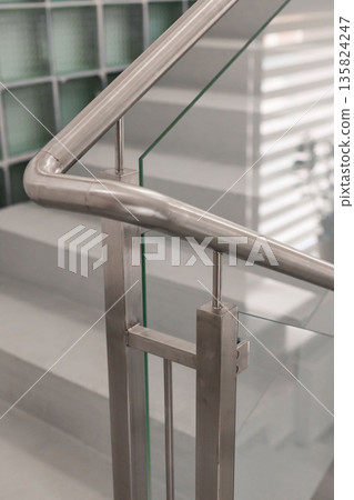 Stainless steel railing meets glass panels at a sleek staircase, showcasing modern architectural design. The light filters through, enhancing the clean lines and elegance Stainless steel railing meets glass panels at a sleek staircase, showcasing modern architectural design. The light filters through, enhancing the clean lines and elegance 135824247