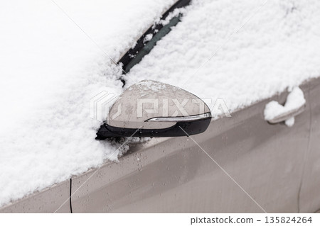 A car parked on a street is covered in snow during winter. The side mirror is almost completely buried beneath the snow. The scene shows the aftermath of a snowstorm A car parked on a street is covered in snow during winter. The side mirror is almost completely buried beneath the snow. The scene shows the aftermath of a snowstorm 135824264