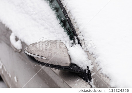 Snow blankets a parked car in a winter parking lot. The scene shows a mirror covered in snow during a heavy snowstorm. Winter weather leads to difficult driving conditions Snow blankets a parked car in a winter parking lot. The scene shows a mirror covered in snow during a heavy snowstorm. Winter weather leads to difficult driving conditions 135824266