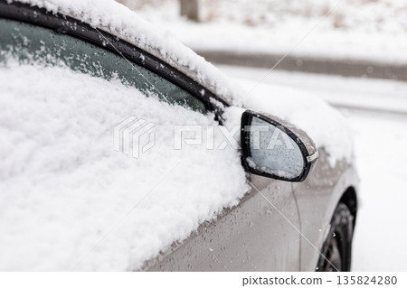 A car is parked on a road. Snow is piled on top of the car and along the windows. It is winter and flakes are falling from the gray sky. Visibility is low due to the snowfall A car is parked on a road. Snow is piled on top of the car and along the windows. It is winter and flakes are falling from the gray sky. Visibility is low due to the snowfall 135824280