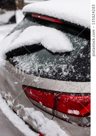 Snow accumulates on the rear windshield of a parked car in a residential area. The scene shows a typical winter day with cold weather and overcast skies Snow accumulates on the rear windshield of a parked car in a residential area. The scene shows a typical winter day with cold weather and overcast skies 135824283
