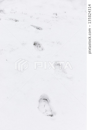 Footsteps are visible in the snow, creating a path across a winter scene. The white ground shows the impact of movement in a cold setting Footsteps are visible in the snow, creating a path across a winter scene. The white ground shows the impact of movement in a cold setting 135824314