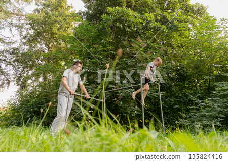 A father and his child are having fun together at a playground, with the child attempting to climb on a bar while the father supports him A father and his child are having fun together at a playground, with the child attempting to climb on a bar while the father supports him 135824416