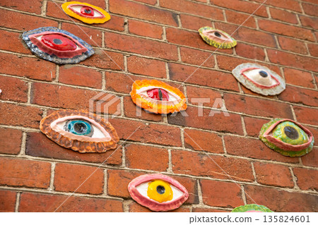 Various eye shapes in different colors are mounted on a red brick wall 135824601