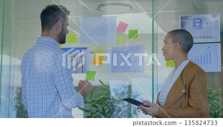 Colleagues adjusting sticky notes and using tablet at office glass wall with charts, security icon Colleagues adjusting sticky notes and using tablet at office glass wall with charts, security icon 135824733