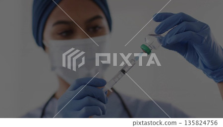 Nurse wearing cap mask and gloves drawing medication into syringe in clinic, with vial stethoscope 135824756