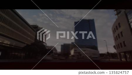 Glass office tower catching dusk light on downtown street, with cars traveling and traffic lights 135824757