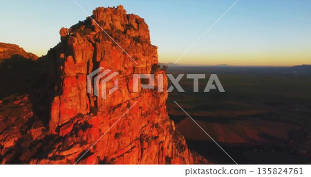 Illuminating red sandstone cliff on desert plateau at sunrise with sparse shrubs, copy space 135824761